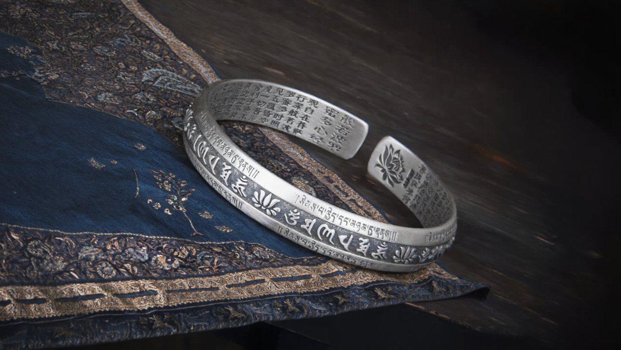 Close-up of a silver Tibetan bracelet showing intricate patterns like the Six-Word Mantra and Endless Knot.